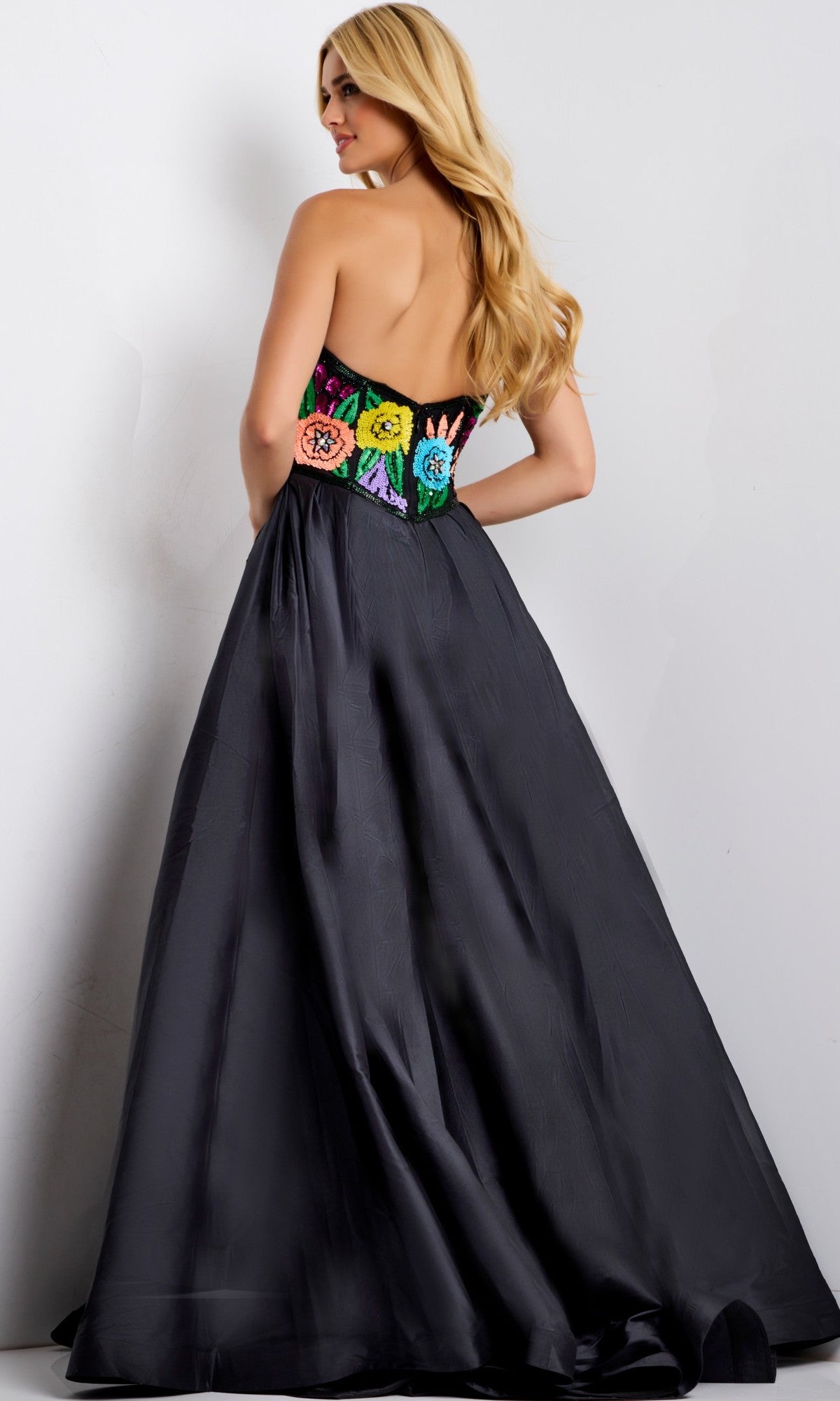 A woman faces away, wearing the Jovani 49233 long prom dress—a strapless ball gown with a floral-beaded bodice and a flowing satin A-line skirt.